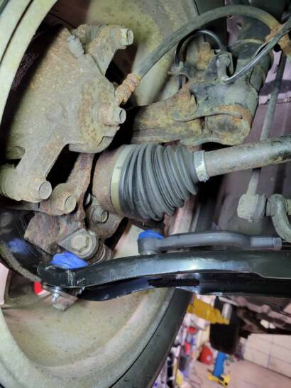 Close-up of a new lower control arm with a new ball joint boot, installed below the CV axle and steering knuckle