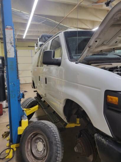 White work van on a two-post lift with the hood open and a front wheel off inside the New Level Auto Service shop in Rockville, MD