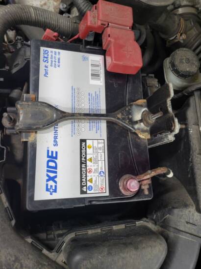 New Exide car battery installed under the hood and held in place with the hold-down bracket at New Level Auto Service in Rockville, MD