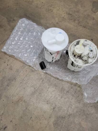 Old and new fuel pump modules side by side on bubble wrap, the new one clean and white, the old one stained from use