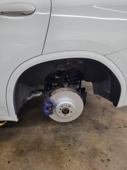 White SUV with the wheel off, showing a new brake rotor and blue brake caliper